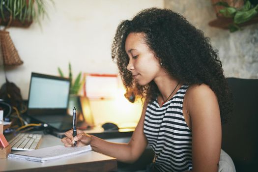 Shot of an attractive young african woman sitting alone and making a note in her home office - Stock photo