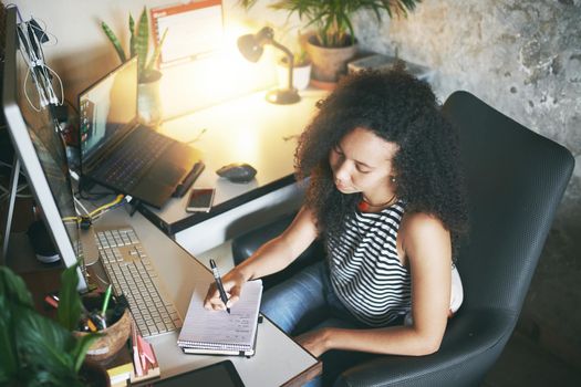 Shot of an attractive young african woman sitting alone and making a note while working from home stock photo