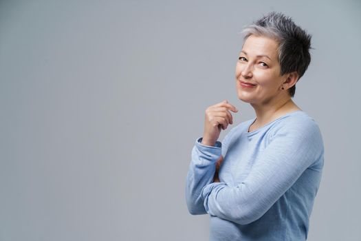 Lovely grey hair mature business woman in 50s posing sideways with hands folded and copy space on right isolated on white background. Copy space and place for product placement. Aged beauty.