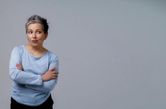 Thoughtful mature woman with grey hair in 50s posing with hands folded and copy space on right isolated on white background. Copy space and place for product placement. Aged beauty. Toned image.