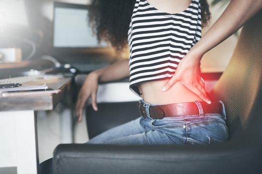 Shot of a young african woman sitting alone and suffering from back ache while using her computer to work from home stock photo