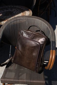 Brown leather backpack on the stylish chair. Outdoor photo