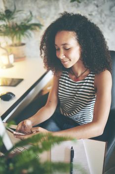 Shot of an attractive young woman sitting alone and using her cellphone while working from home stock photo