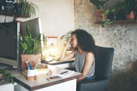 Shot of an attractive young african woman sitting alone and feeling stressed while using her computer to work from home stock photo