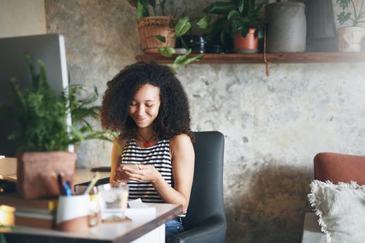 Shot of an attractive young african woman sitting alone and using her smartphone to work from home stock photo