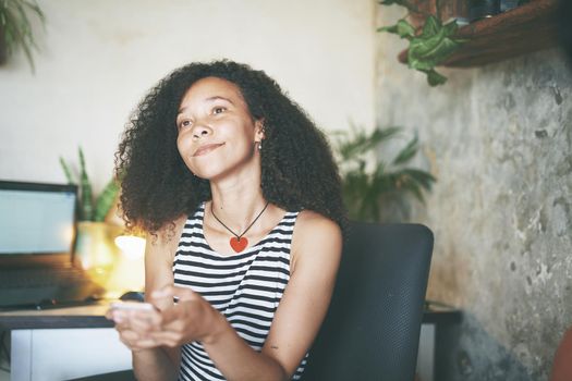 Shot of an attractive young woman sitting alone and using her cellphone while working from home stock photo