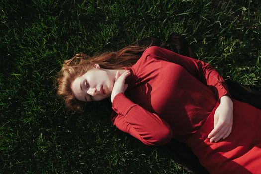 a blonde girl in red lies on the grass in the summer and enjoys the weather