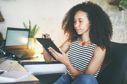 Shot of an attractive young woman sitting alone and using her tablet while working from home stock photo