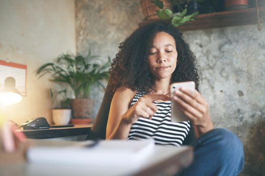 Shot of an attractive young african woman sitting alone and using her cellphone while working from home stock photo