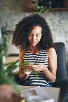 Shot of an attractive young african woman sitting alone and using her smartphone to work from home stock photo