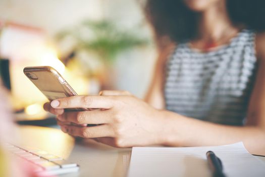 Shot of an unrecognizable young woman sitting alone and using her cellphone to work from home stock photo