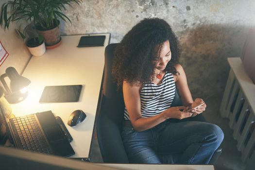 Shot of an attractive young african woman sitting alone and using her cellphone while working from home stock photo