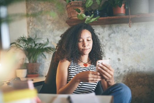 Shot of an attractive young woman sitting alone and using her cellphone while working from home stock photo