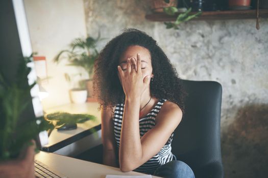 Shot of an attractive young african woman sitting alone and feeling stressed while using her computer to work from home stock photo