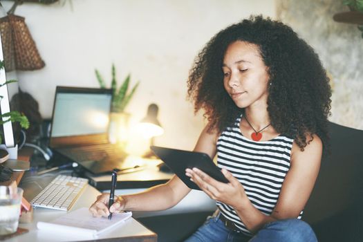 Shot of an attractive young woman sitting alone and using her tablet while working from home stock photo