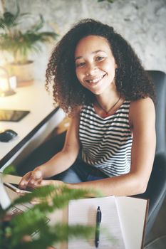 Shot of an attractive young african woman sitting alone smiling at the camera while working from home stock photo