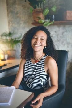 Shot of an attractive young woman sitting at her desk smiling at the camera - Stock Photo