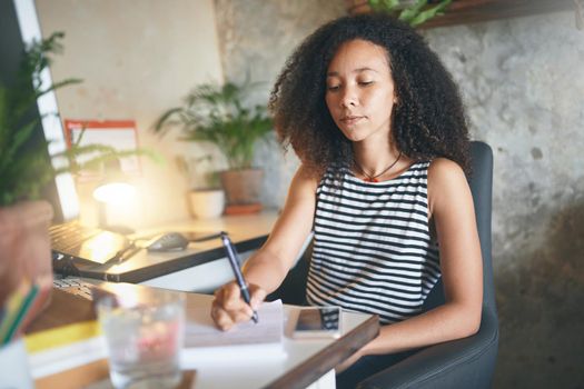 Shot of an attractive young african woman sitting alone and making notes in her home office - stock photo