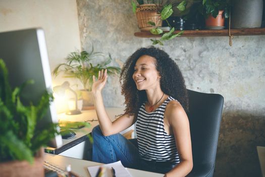 Shot of an attractive young african woman sitting alone and using her computer for a video chat while working from home stock photo