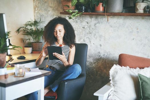 Shot of an attractive young african woman sitting alone and using her tablet while working from home stock photo