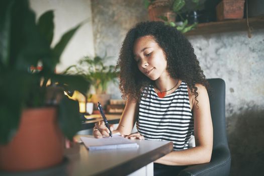 Shot of an attractive young african woman sitting alone and making a note while working from home stock photo