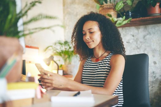 Shot of an attractive young woman sitting alone and using her cellphone to work from home stock photo