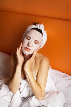 Young girl with clean skin with a mask on her face, lying in bed, resting after a shower, relaxing at home. Close-up