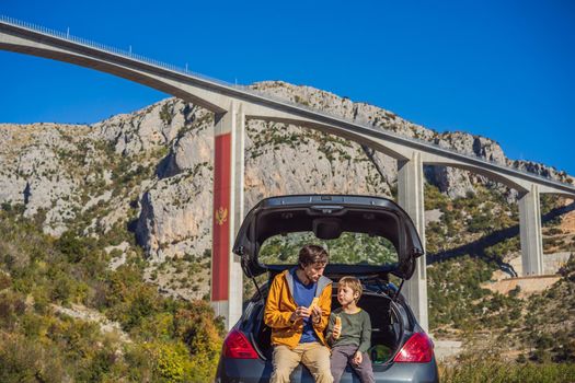 Montenegro. Dad and son tourists are sitting on the trunk of a car. Road trip around Montenegro. Bridge Moracica. Reinforced concrete bridge across the Moraci gorge. The motorway Bar - Bolyare. The bridge is on the Smokovac - Uvach - Mateshevo section. The Moracica Bridge was built by the China Road and Bridge Corporation.