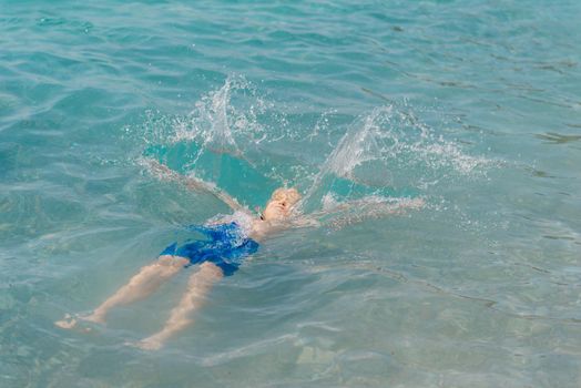 Child learning to swim in the open sea of tropical resort. Kids learn swimming. Exercise and training for young children. Little boy with colorful float board in sport club. Swimming baby or toddler. Happy child boy swims in sea in swimming circle with splash. Blue sky and water. Swimming training. Fun joy activities on vacation in the beach. Childhood moments lifestyle. Freedom careless. boy swim in the sea.