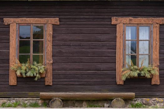 The facade of an old wooden house with two windows and a bench.