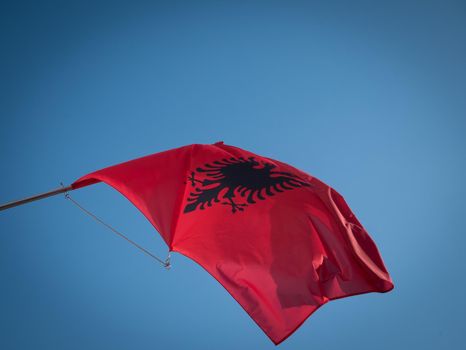 The Albanian flag flying on a pole with blue background