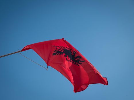 The Albanian flag flying on a pole with blue background