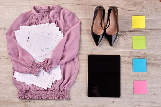 Top view flat lay pink blouse with work papers and shoes. Tablet with sticky notes on the desk.