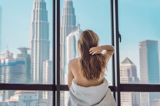 Woman wakes up in the morning in an apartment in the downtown area with a view of the skyscrapers. Life in the noise of the big city concept. Not enough sleep.