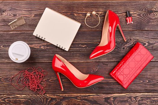 Flat lat red female accessories and blank notepad for copy space. Brown wooden desk background.