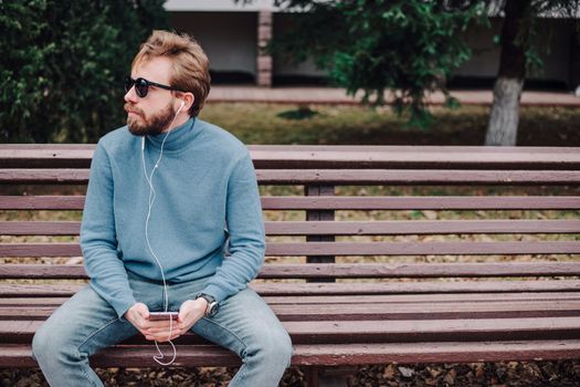 young hipster gay man listening music with headphones siting in a park