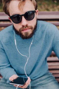 young hipster gay man listening music with headphones siting in a park