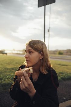 blonde girl eating pizza sitting outside at sunset