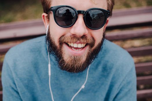 young hipster gay man listening music with headphones siting in a park