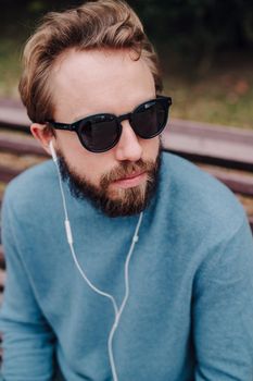 young hipster gay man listening music with headphones siting in a park