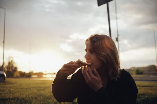 blonde girl eating pizza sitting outside at sunset