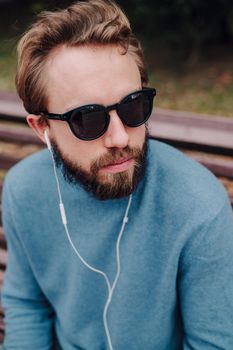 young hipster gay man listening music with headphones siting in a park