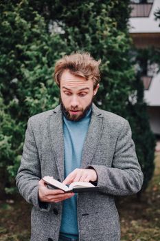 Portrait handsome bearded man wearing glasses blue shirt.Man near university library, reading book and relaxing. Blurred background.Horizontal, film effect.