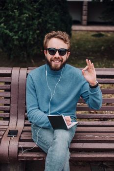 young gay hipster boy notice ideas siting in a park and listen music by headphones