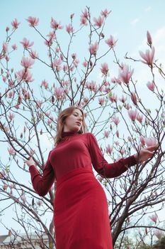 a veth-haired girl in red against the background of a magnolia tree. the concept of unity with nature