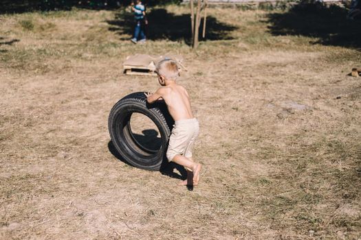 the boy with bare torso playing with the old tire wheel outdors in the village