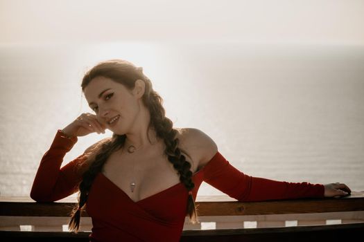 Closeup video portrait of sensual young brunette woman in red dress, happily dancing outdoors isolated on blurry sea background with natural bokeh in soft warm sunset backlight