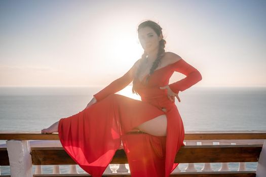 Closeup video portrait of sensual young brunette woman in red dress, happily dancing outdoors isolated on blurry sea background with natural bokeh in soft warm sunset backlight