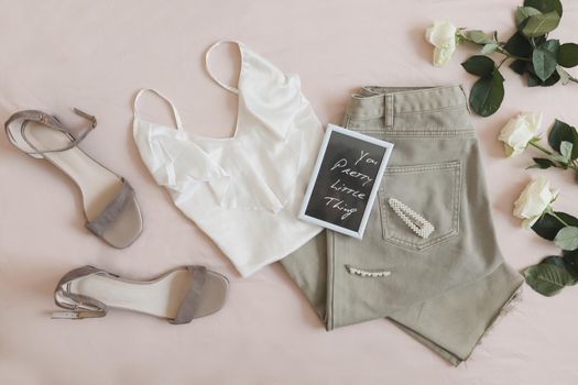 Jeans, sandals and bouquet of flowers on beige background. Overhead view of female casual spring summer outfit. Trendy stylish women clothes. Flat lay, top view