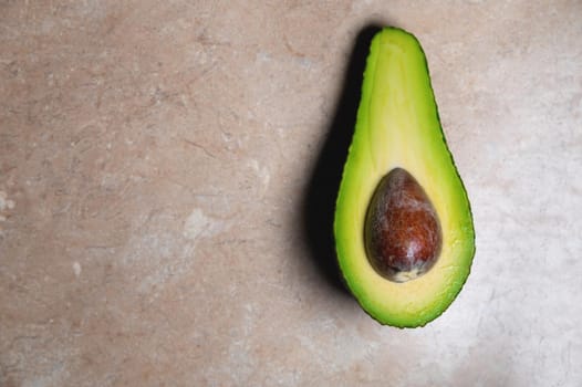 background. cut avocado in half, with a bone inside, lies on the table. view from above.